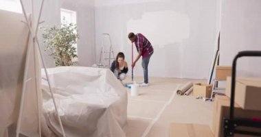 Bir daireyi bitirmek için birlikte çalışan iki neşeli genç ellerinde boya silindirleri, kutuların etrafındaki beyaz boyalarla kirleniyorlar. Duvarları boyayan arkadaşlar.