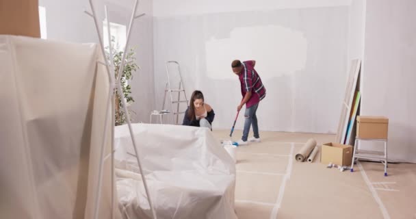 손에 페인트 롤러를 들고 있는 아파트를 완성하기 위해 함께 일하고 있는 두 명의 활달 한 젊은이들 이 흰색 페인트를 손에 들고 사다리 친구들 이 벽에 페인트를칠 하면서 더러워지고 있습니다 — 비디오