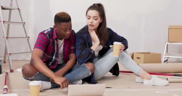 İç mimar mimarlar yeni inşa edilmiş apartman inşaatında çalışıyorlar. Genç kadın ve iş arkadaşı kahve fincanları dolusu dizüstü bilgisayarla yerde oturuyor. — Stok video
