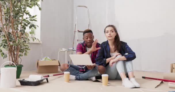 Casal está gastando tempo em novo apartamento redecorando paredes de pintura quarto pintura acessórios espalhados ao redor amantes está navegando através de inspirações no laptop encomendar móveis, high-five — Vídeo de Stock