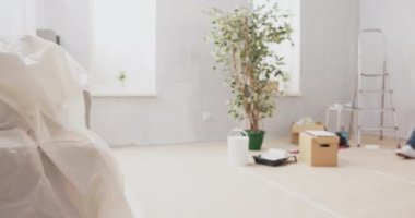 Tadilat sırasında duvarları boyarken bir apartman manzarası. İki insan yerde oturmuş kahve içiyor ve tablet oda, mobilya, dekorasyon gibi ilhamlar alıyor.