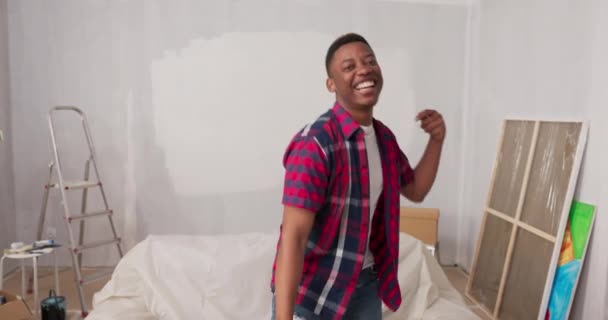 Um homem olha para a câmera com um rosto orgulhoso, sorrindo, no fundo uma parede pintada recentemente renovado apartamento, arquiteto, pintor, decorador, um menino dançando brincando com a felicidade — Vídeo de Stock