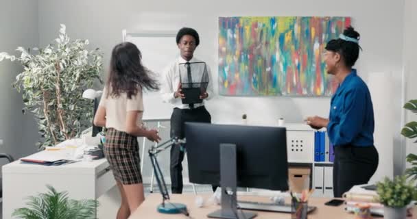 Vicces munkatársak szórakoznak a céges munka szünetében, egy fehér inges férfi kukát tart, a nők összetört papírral céloznak rá, kosárlabdával az irodában. — Stock videók