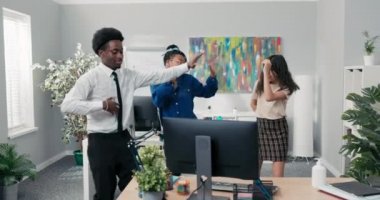 İşte, ofiste, işte, işte, iş partisinde, iş partisinde, iki kız ve kravat takmış bir adam birlikte dans ediyor, gülüyor, gülümsüyor, stres atıyor, bilgisayardan müzik çalıyor.