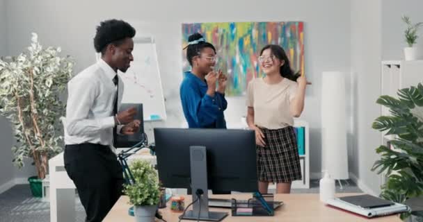 Baile en el trabajo, oficina, descanso de deberes, fiesta de empresa, dos chicas y un hombre en camisa y corbata bailando juntos, tonteando, riendo, sonriendo, aliviando el estrés, tocando música desde la computadora — Vídeo de stock