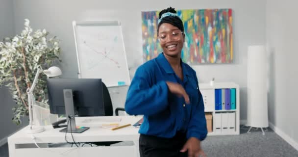 Elegante chica luchadora vestida con camisa azul y gafas con estilo, bailando en medio de la oficina, agitando sus brazos hacia adelante, feliz por el éxito de la empresa, mujer de negocios con una sonrisa en la cara — Vídeos de Stock