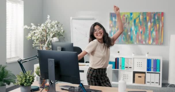 En vakker kvinne danser på et kontor, et firma, et firma mellom pultene til kollegene, hun er glad, smilende, hun avslutter jobben tidlig, får en forfremmelse, endrer stilling – stockvideo