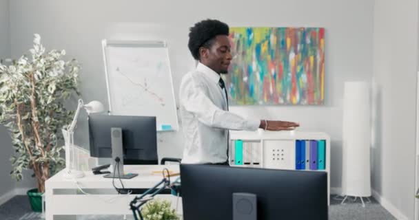 Ein Mann mit Afro tanzt inmitten eines Firmenbüros, freut sich über einen Vertrag, gute Nachrichten, fröhlicher Mitarbeiter bekommt eine Beförderung, beendet die Arbeit früher, höhere Bezahlung — Stockvideo