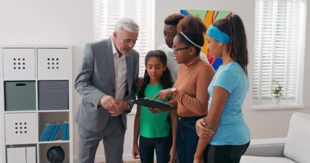 Inspección con agente de bienes raíces de nuevo apartamento en el centro de la ciudad pareja con niños deciden comprar piso para alquilar juntos consultan expertos hojear los diseños de la casa en la tableta mirar en la habitación renovada — Vídeos de Stock