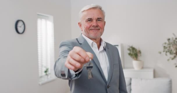 Schuss Wohnungsschlüssel auf Handfläche in Richtung Kamera ausgestreckt, grauhaariger älterer Mann im Anzug übergibt Schlüssel, Immobilienmakler, Wohnungseigentümer gibt Raum zur Nutzung — Stockvideo