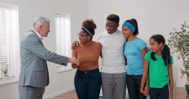 Homem mais velho com cabelos grisalhos, agente imobiliário vende apartamento para jovem casal com filhos, mãos mulher as chaves, eles sorriem, momento feliz — Vídeo de Stock