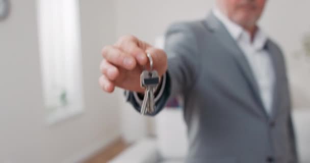 Shot of apartment keys extended on palm of hand toward camera, gray-haired mature man dressed in suit hands over keys, real estate agent, owner of apartment, gives room to use — Stock Video
