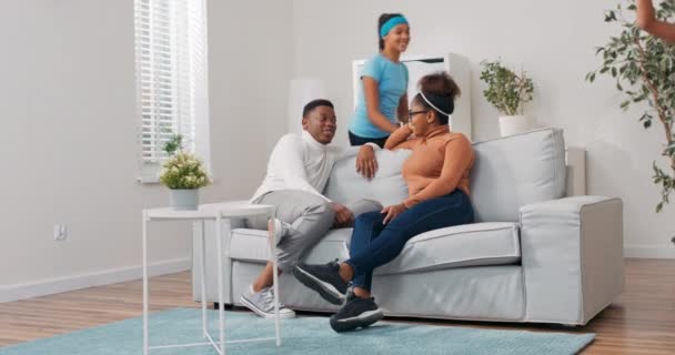 Ett ungt par sitter på soffan i lägenheten, de diskuterar visioner planerar att renovera ett rum, mannen presenterar idéer för kvinnan, barnen springer runt dem, killen pekar på sina döttrar, skrattar — Stockvideo