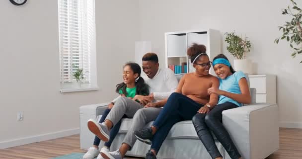 Parents playing with their daughters, family spending time together on a day off, running towards the couch and sitting on it at the same time, hugging, embracing, smiling — Stock Video