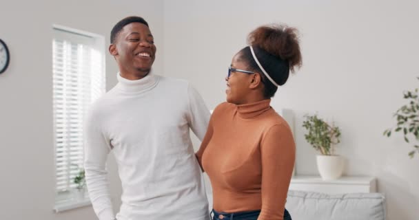 A couple in love moves into a new apartment, cardboard boxes with packed things stand in the living room, the man embraces his beloved, they smile — Stock Video