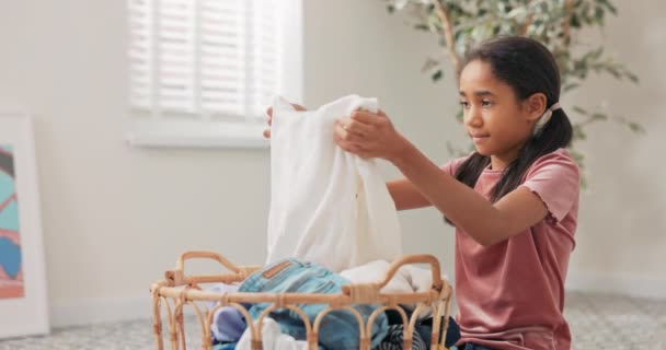 A smiling pretty girl sits in the middle of the bathroom, laundry room, in front of a large wicker basket filled with colorful clothes in hands, daughter helping mother with household chores — Stock Video