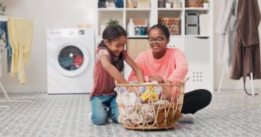 Gözlüklü, gülümseyen olgun bir kadın bir sepet dolusu çamaşırla banyo zemininde oturuyor, kızı etrafta oynaşıyor, annesi tarafından oynanıyor, kıyafetlerini kafasının üstüne fırlatıyor.