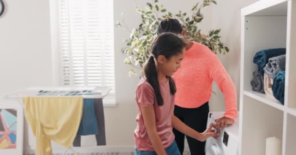 La madre pasa tiempo con su hija en la sala de lavandería, baño, enseña a las niñas a realizar tareas domésticas, explica el funcionamiento de la lavadora, programa de conjuntos de niños por sí misma, abrazo con la mamá — Vídeos de Stock