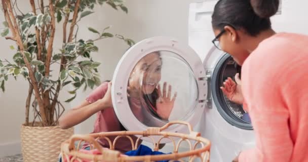 Обманывать, шутить, играть во время выполнения домашних работ, женщина и девушка тусуются в прачечной, ванной комнате, показывая глупые лица друг другу через дверь стиральной машины — стоковое видео