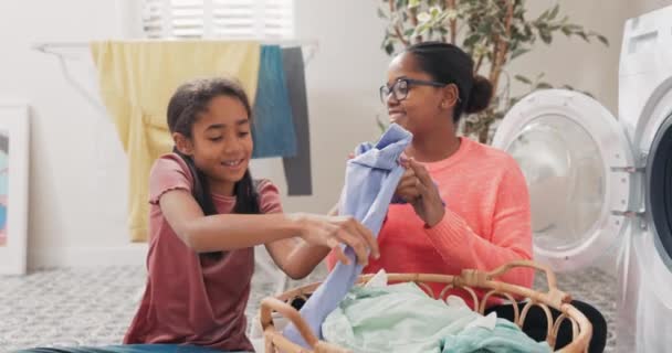 Улыбающаяся женщина и ее дочь, вытаскивая одежду из корзины для белья и загружая ее в барабан стиральной машины, девушка помогает с домашними делами — стоковое видео