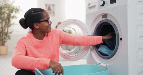 A woman is sitting on the floor unpacking a drum, taking clean fresh smelling clothes out of the washing machine which she puts into a bowl in the background a little girl is sitting on the couch — Stock Video