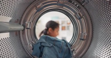 Çamaşır makinesinin içinde, küçük bir kız renkli giysileri varile koyar, annesine ev işlerinde yardım eder.