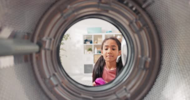 Inside the washing machine, a little girl opens the door and puts colorful clothes into the drum, she helps her mother with household chores — Stock Video