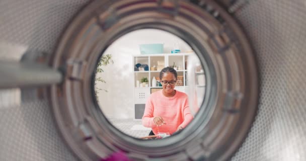 Una vista desde el interior del tambor de una mujer joven divirtiéndose mientras ayuda con las tareas domésticas, lanzando distancias de ropa en la lavadora y tratando de apuntar, feliz de tener éxito — Vídeos de Stock