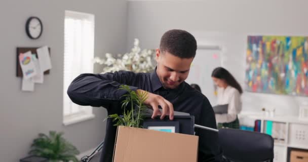 Чоловіка підвищують на нову посаду він стоїть посеред офісу на задньому плані робочого столу хлопчик тримає в руках картонну коробку з упакованим ноутбуком, особисті речі, він посміхається щасливий — стокове відео