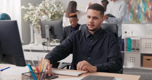 Χαμογελώντας τύπος ντυμένος με μαύρο πουκάμισο κάθεται στο γραφείο μπροστά από έναν υπολογιστή, παίρνει μια κλήση στο smartphone, μιλάει στον καλούντα για τα καλά νέα, διαβιβάζει τα νέα στην εταιρεία, και ο καθένας χαίρεται — Αρχείο Βίντεο
