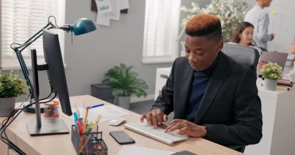 Κομψός άνθρωπος που εργάζεται σε ένα αγόρι γραφείο κάθεται πίσω από το γραφείο μπροστά από τον υπολογιστή, τον έλεγχο της ορθότητας του χαρτιού και των ηλεκτρονικών εγγράφων, εισάγοντας δεδομένα στο σύστημα χτυπώντας δάχτυλα στο πληκτρολόγιο — Αρχείο Βίντεο
