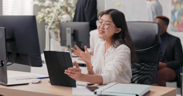 Μια γυναίκα με λευκό πουκάμισο και γυαλιά κάθεται στο γραφείο κρατώντας ένα δισκίο στα χέρια, αυτή έχει συνομιλία βίντεο με το αφεντικό μέσω μιας κάμερας, συζητούν τις λεπτομέρειες της συνεργασίας casual chat — Αρχείο Βίντεο
