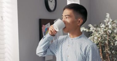 Şirketin ciddi bir şekilde odaklanmış düşünceli başkanı, iş adamı pencerenin kenarındaki şirketin ofisinde duruyor, panjurlarla kaplanmış ve içine bakıyor, işi düşünüyor.