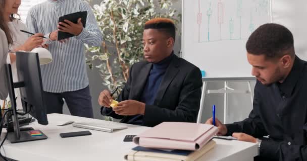 Medewerkers van het bedrijf werken samen aan een computerplanning, organiseren, een project, een man in een garnering neemt plakkerige notities in zijn hand en plakt ze op de monitor — Stockvideo