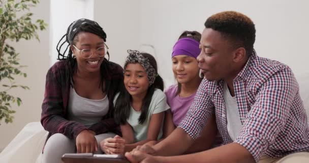 En glad familie sidder på sofaen i lejlighed under renovering ægtepar og deres to døtre gennemse tabletten for inspiration til, hvordan du afslutter værelserne på udkig efter maling farver – Stock-video