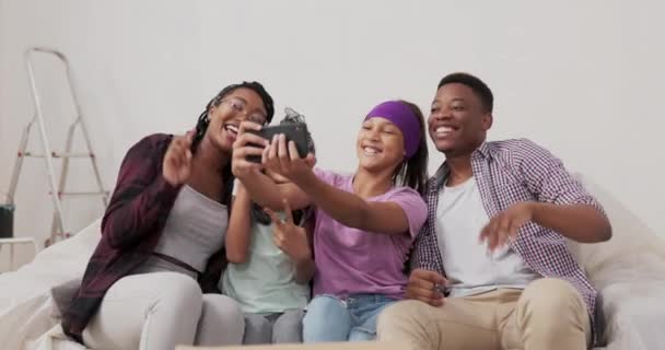 Uśmiechnięta piękna dziewczyna nagrywa wideo z telefonem do przyjaciół wraz z rodzicami i siostrą machają ręką w powitaniu z nowego odnowionego mieszkania, do którego się wprowadzili. — Wideo stockowe