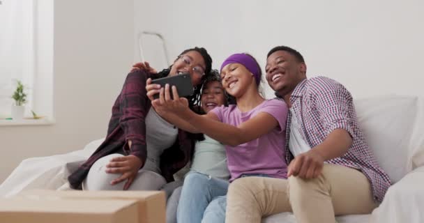 Piękna dziewczyna siedzi na kanapie z rodziną w odnowionym mieszkaniu robi selfie z rodzicami i siostrą ze smartfonem każdy uśmiecha się wskazuje najlepsze zdjęcia posty w mediach społecznościowych — Wideo stockowe