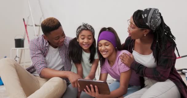 Radostní rodiče a jejich dcery sedí na patře bytu, který právě zrekonstruovali prohlížení místnosti inspirace na tabletu si vybrali barvu stěny pro dětský pokoj-plácání — Stock video