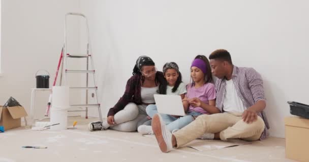 Szczęśliwa rodzina siedzi na podłodze zakupionego mieszkania właśnie odnowione inspiracje pokoju przeglądania na laptopie wybierając kolory farby do ścian omawiając ich wizję wykończenia. — Wideo stockowe
