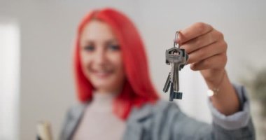 Kameraya doğru genişletilmiş daire anahtarları, takım elbiseli pembe saçlı kadın evrakları tutuyor ve anahtarları teslim ediyor, emlakçı, apartman sahibi, kullanım odası sahibi.