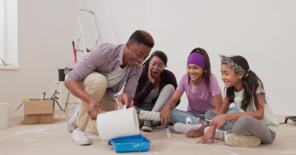 La famille est assise dans la chambre en cours de rénovation papa verse de la peinture blanche dans le plateau les filles vont peindre des murs ils attrapent des rouleaux et des brosses dans leurs mains et se mettent au travail avec des sourires de joie — Video