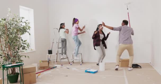 Őrült, szoros családi festmények falak fehér festék segítségével görgők táncolnak a szoba közepén énekelnek szülők játszanak a gyerekekkel a ház kész felújítás — Stock videók