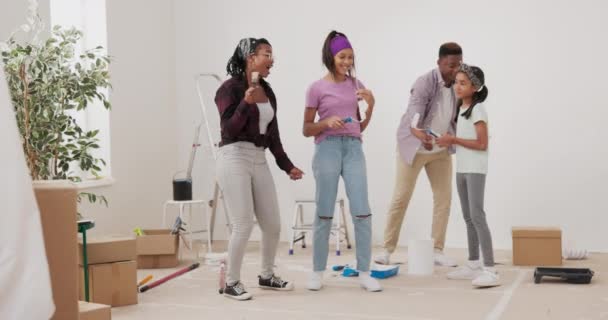 Безумная счастливая семья краски стен белой краской с кисточками они танцуют в середине комнаты поют родители играют с детьми дом готов к ремонту — стоковое видео