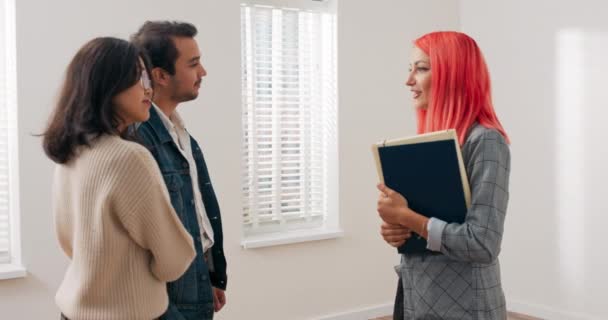 Viendo apartamento en venta, alquiler a inquilinos potenciales, pareja joven está hablando en la habitación con agente de bienes raíces, están discutiendo haciendo preguntas negociando precio mujer está tratando de dar respuestas — Vídeos de Stock