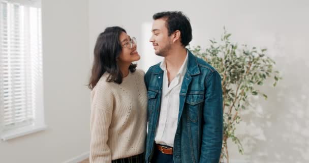 Pareja joven en el amor alquiler de comprar su primer apartamento juntos alegre sonriente mujer abraza novio en la mano sosteniendo las llaves de piso que están en medio de una habitación vacía recientemente renovado — Vídeos de Stock