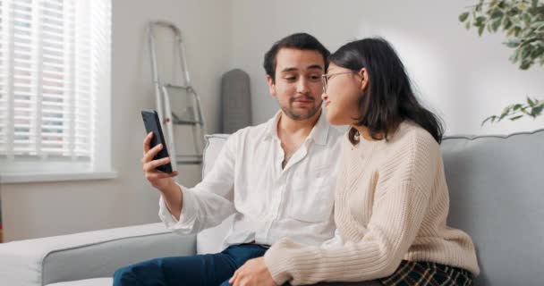Birbirine aşık genç bir çift yeni evlerinde oturup telefona bakıyor, internetten mobilya arıyor, dekorasyon yapıyor, ilham seçimini düşünüyor. — Stok video