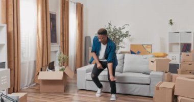 Mutlulukla dolu yakışıklı adam yeni dairede dans ediyor karton kutuları oturma odasına dağıtıyor koreografi ritmik hareketleri uyguluyor.