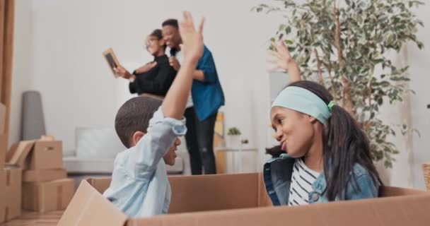Kardeşler taşınmadan arta kalan büyük bir karton kutunun içinde oturuyorlar. Çocuklar sarılıp oynuyorlar. Arka planda gülüyorlar. — Stok video