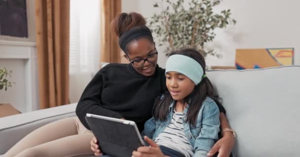 School-age dziewczyna siedzi na kanapie pokazuje mama inspiracji dla jej nowy pokój gry przegląda internet na tablet kobieta obejmuje i uważnie obserwuje, co córka robi — Wideo stockowe