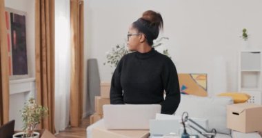 Yeni apartman dairesine taşındıktan sonra tatmin olan kadın, online mobilya arayışında mobilya eksikliği nedeniyle karton kutuların üzerinde duran dizüstü bilgisayarını kullanıyor.
